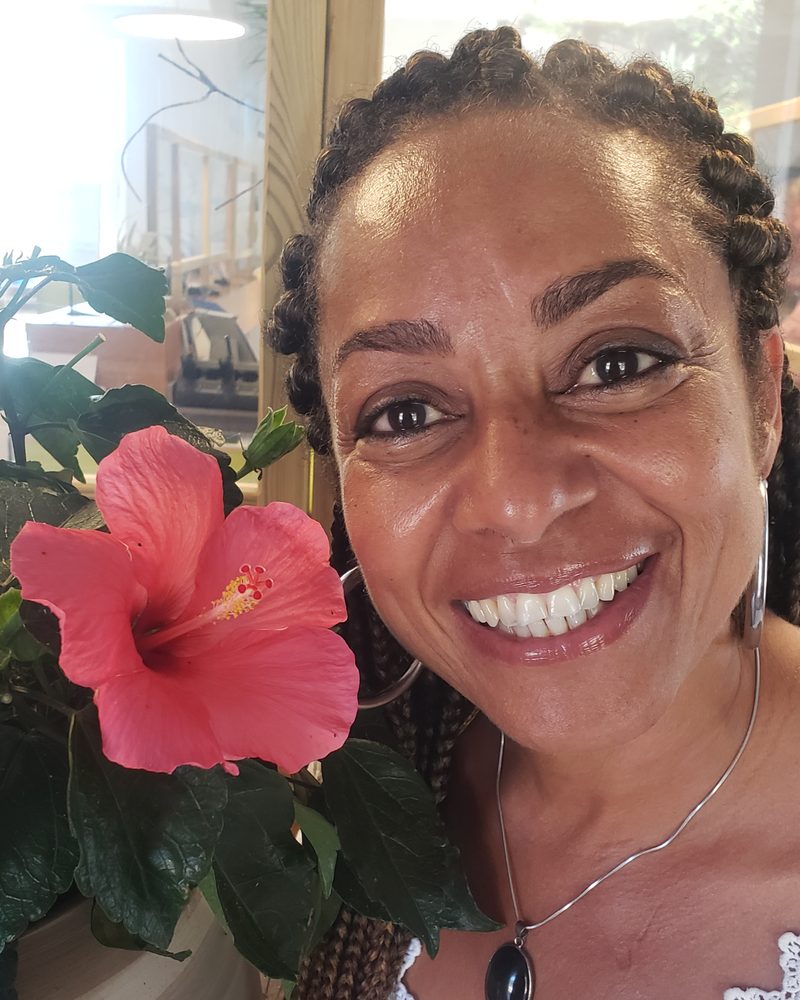 Rosana Maia, souriante, à côté d’un hibiscus en fleur